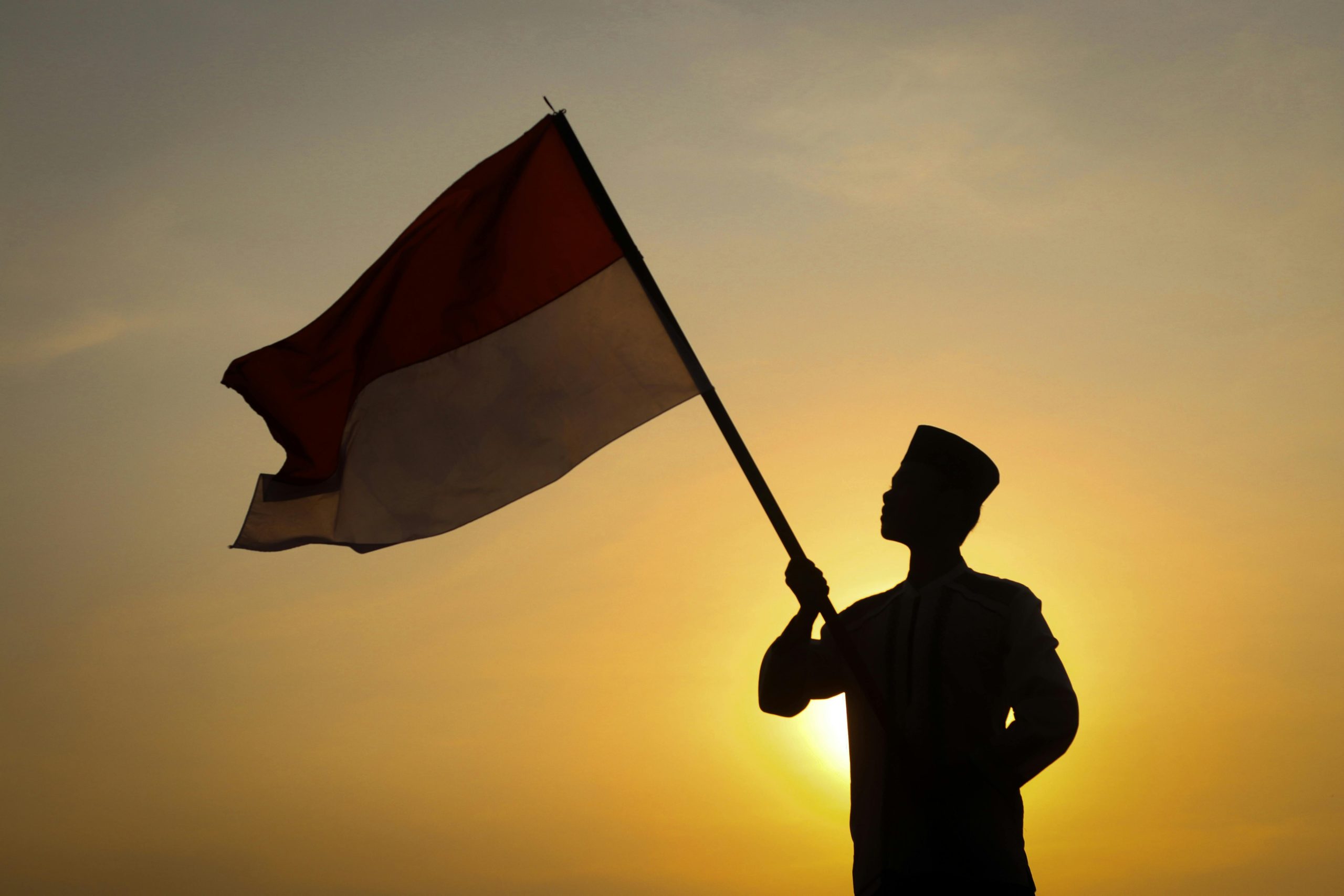 Home Silhouette of individual waving Indonesian flag during a vibrant sunset, symbolizing national pride.