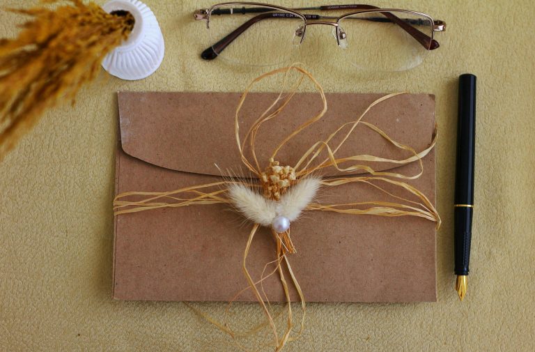 A flat lay of a decorated brown envelope with glasses and pen on a textured surface.