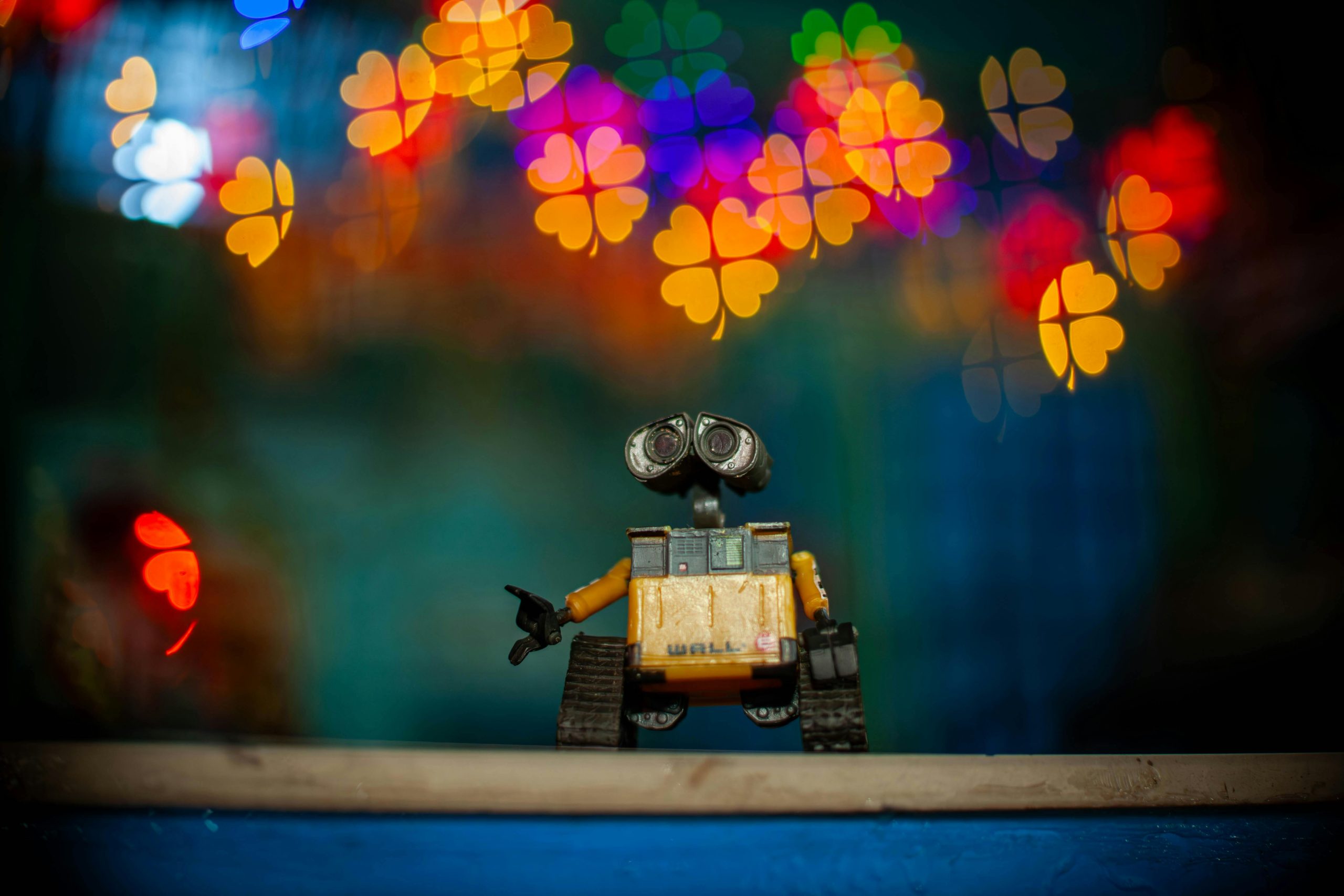 Toy Wall-E figure against vibrant heart-shaped bokeh lights background. Creative composition.
