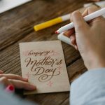 Close-up of a person designing a Mother's Day card with calligraphy on wooden table.